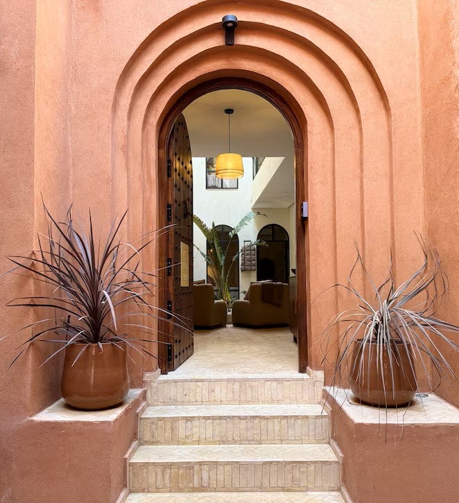 Riad Ambre entrance, a triple scalloped arch in rose ochre plaster opening onto the courtyard