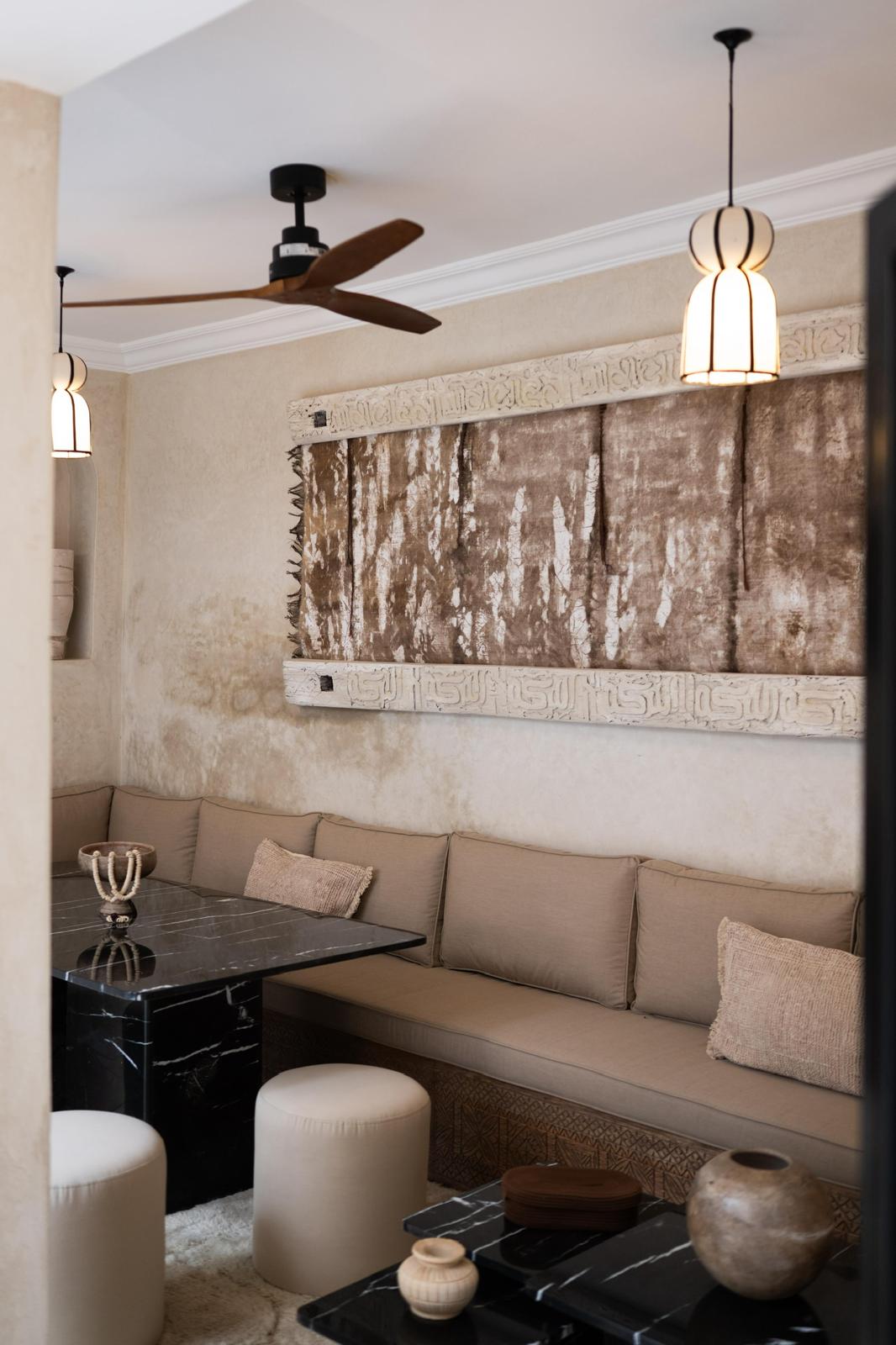 Kasbah Lover salon with a banquette, black marble tables and a framed textile artwork under a carved frieze