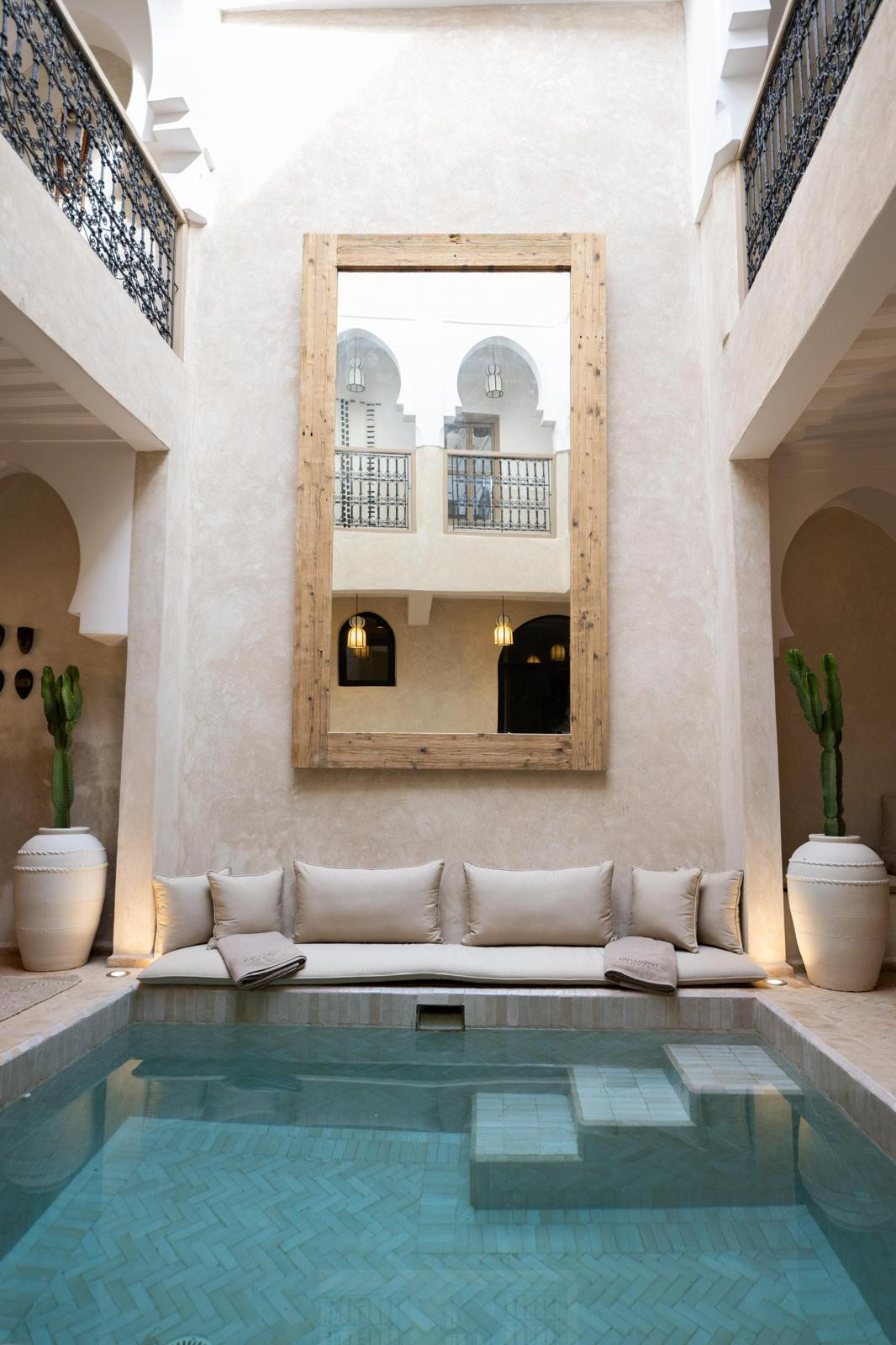 Kasbah Lover courtyard pool with a long bench, cactus jars and a large wooden-framed mirror