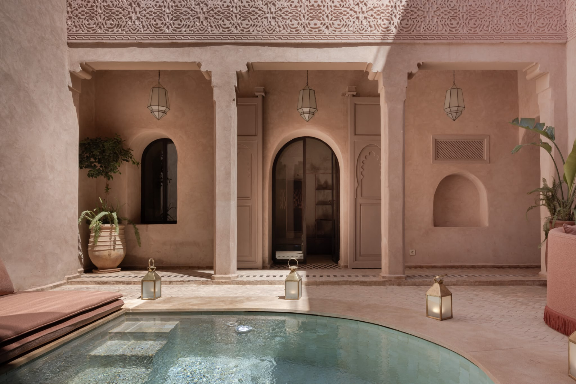 Riad Beij courtyard facade with carved plaster frieze, hanging lanterns and the pool at dusk