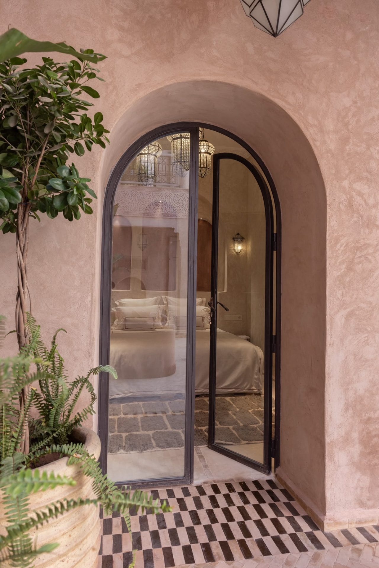 Arched glass doorway of a Riad Beij bedroom, pink lime plaster and checkered zellige floor