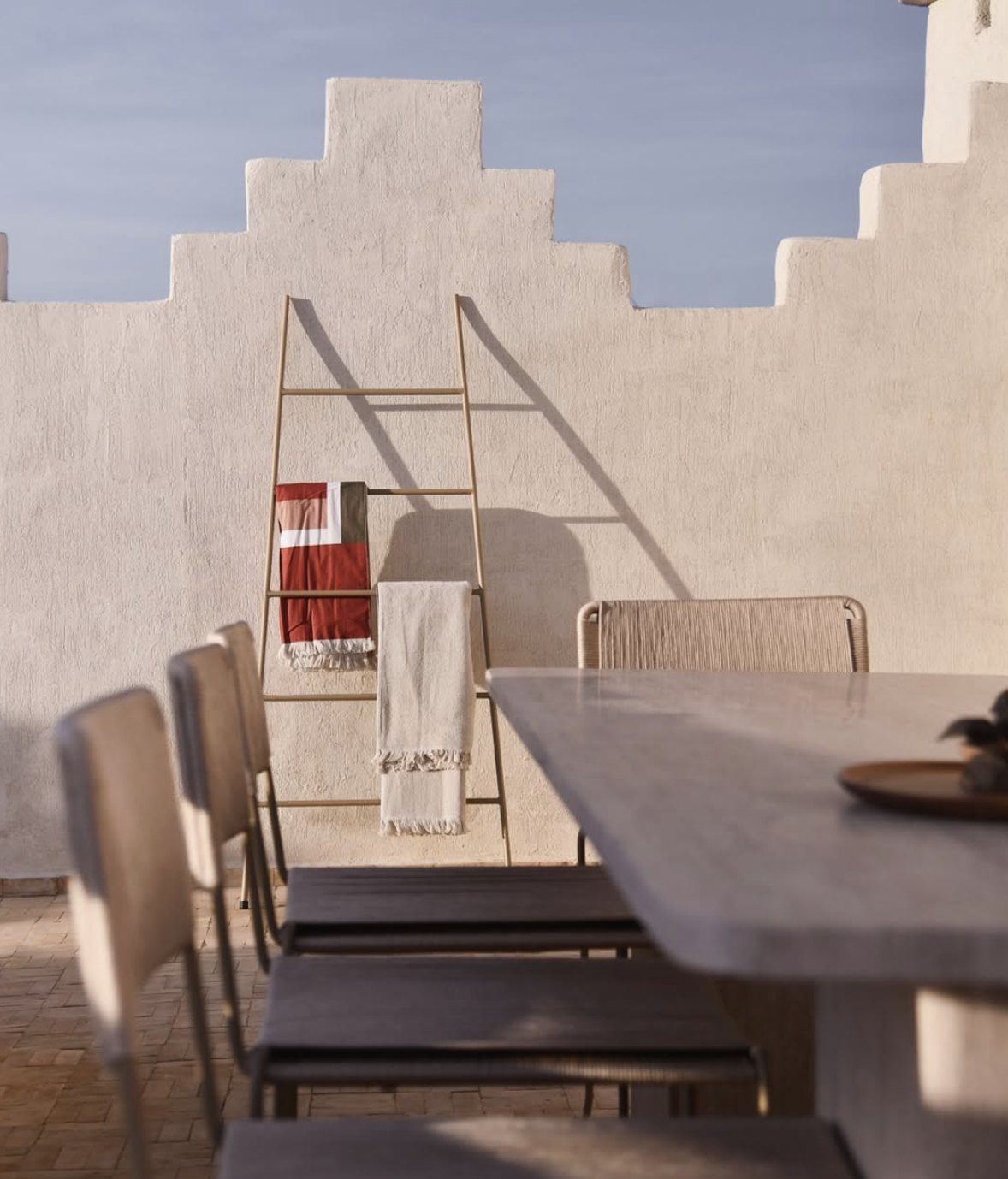 Riad Japandi rooftop terrace with stepped white walls, a dining table and a brass towel ladder