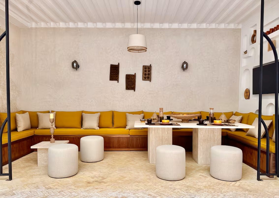 Riad Ambre dining salon with an L-shaped saffron banquette, stone table and white poufs