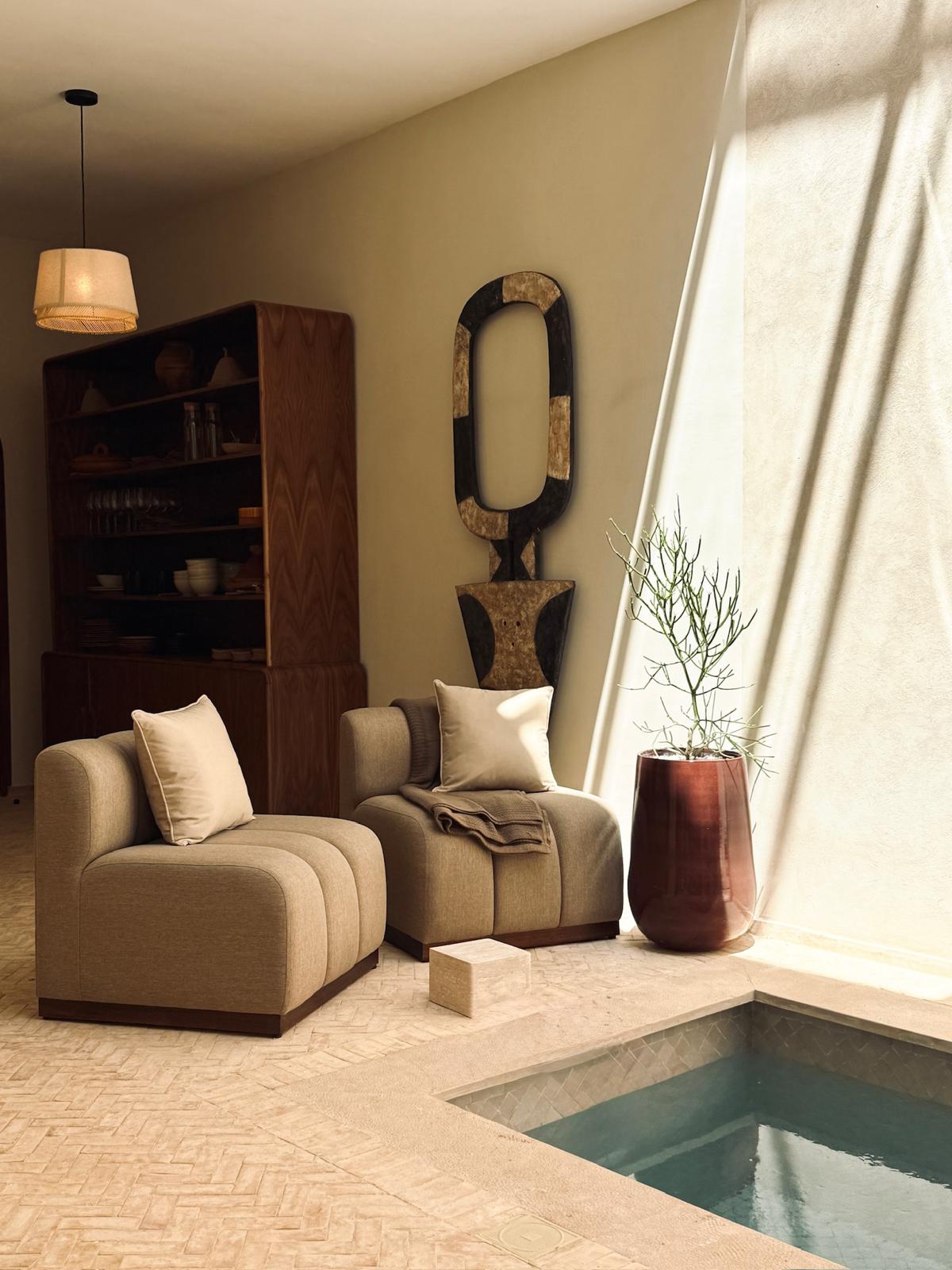 Riad Ambre poolside lounge with low beige armchairs, a dark wood bookcase and a linen curtain
