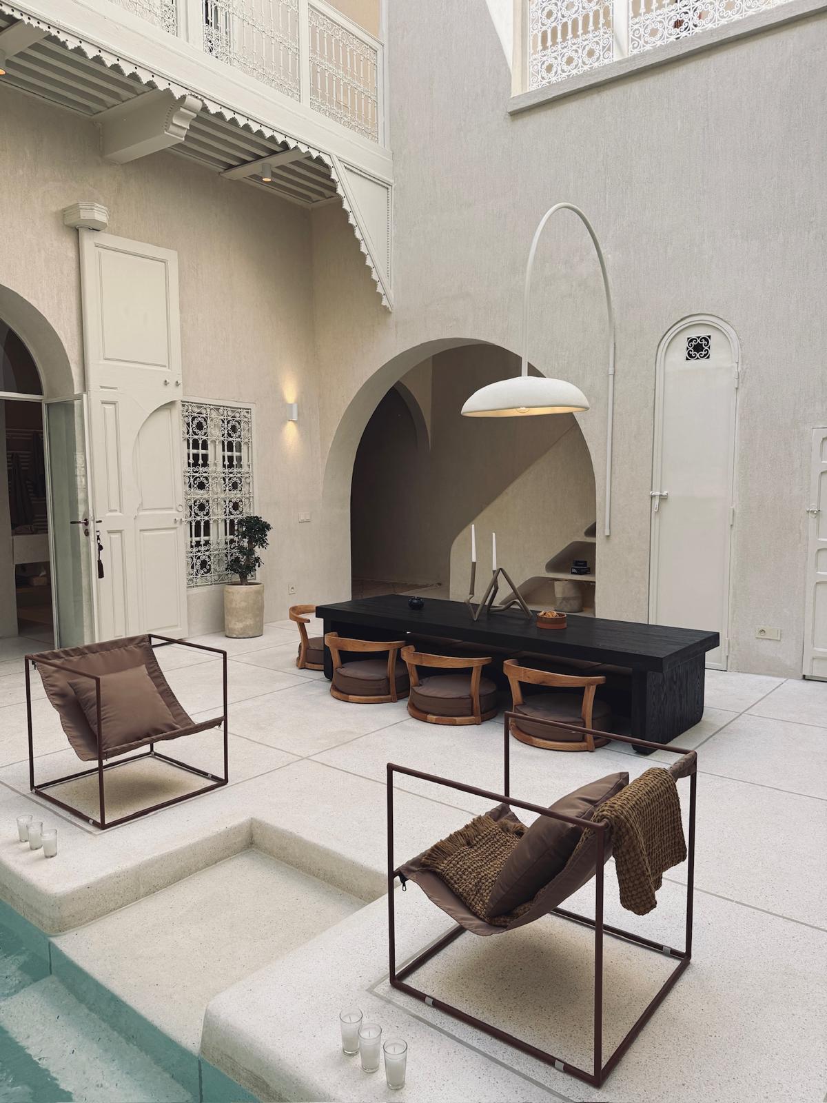 Riad Japandi courtyard with a black dining table, arched niche and white pendant lamp beside the pool